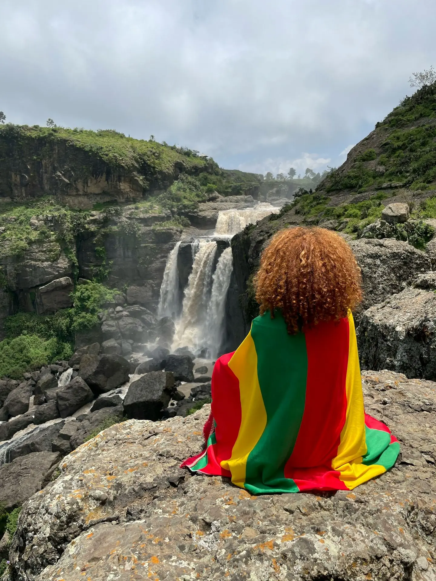 a person sitting on a rock with a waterfall in the background