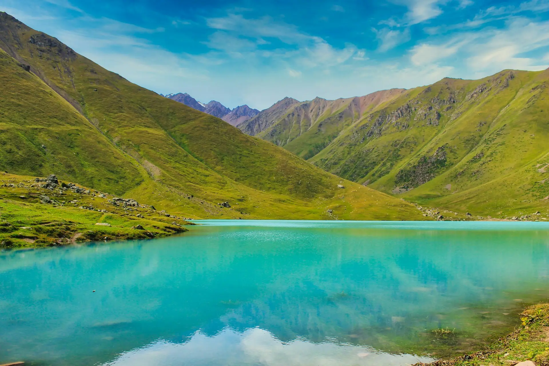 green mountains beside body of water under blue sky during daytime